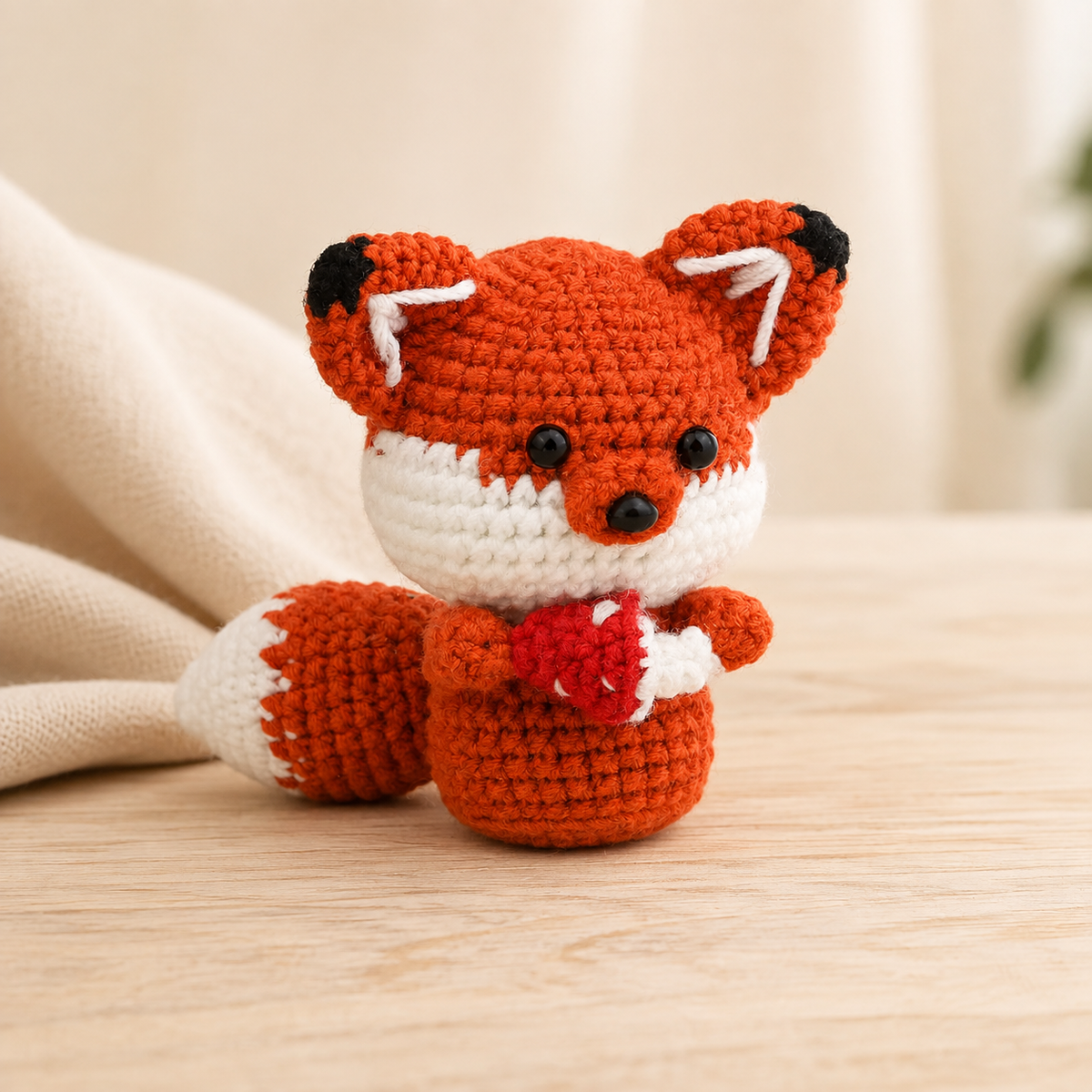 Roter gehäkelter Fuchs mit Herz in warmer Premium-Produktfotografie
