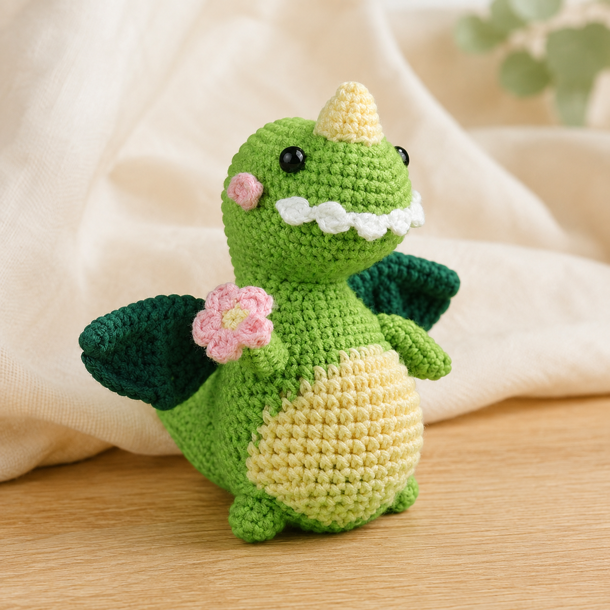 Grüner gehäkelter Dinosaurier mit dunklen Flügeln und rosa Blume in Premium-Produktfotografie